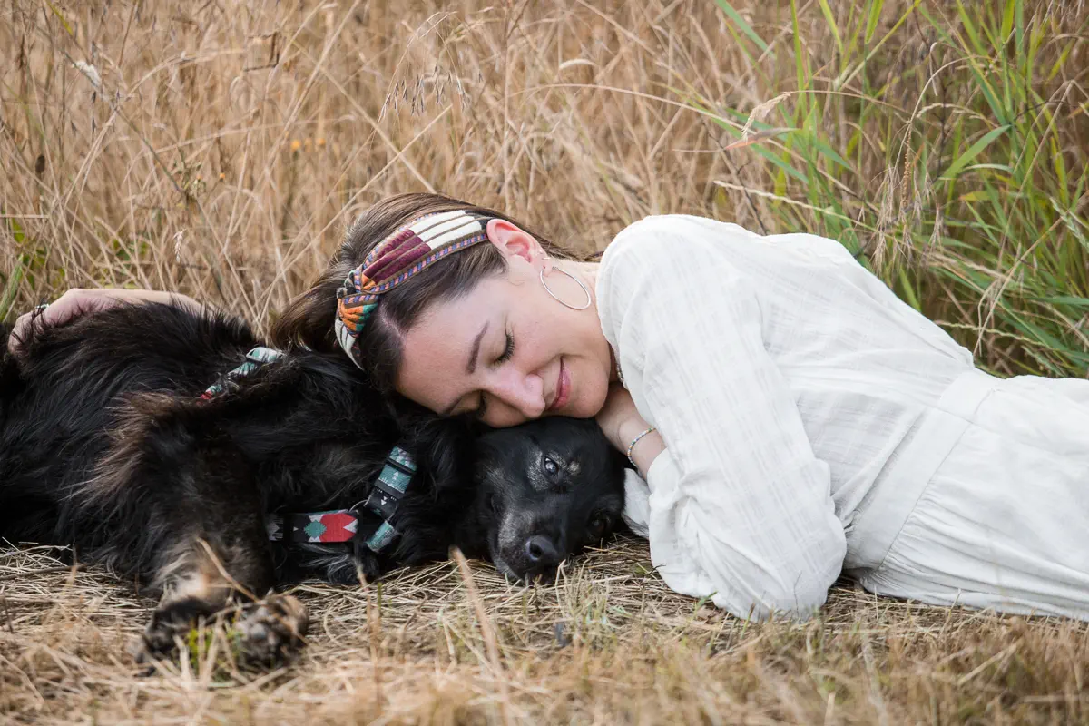 Besitzerin kuschelt ihren Hund im Liegen im Gras